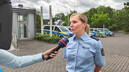 Eine Polizistin wird mit einem WDR-Mikrofon interviewt, im Hintergrund stehen Streifenwagen.