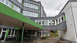 Ein Schulgebäude mit dunkelgrauen Kacheln und grünen Aussenwänden ist verbunden mit einem weißen Gebäude, durch einen Verbindungsgang