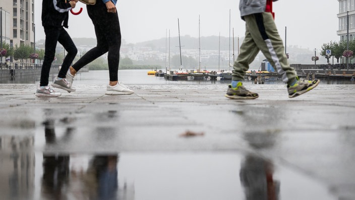 Spaziergänger laufen bei Regen am Ufer des Phoenix Sees in Dortmund