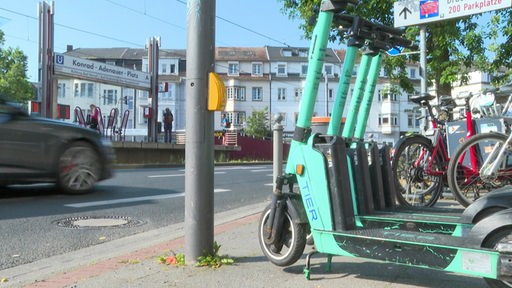 Vier mintfarbene E-Scooter der Firma TIER stehen aufgereiht am Konrad-Adenauer-Platz in Bonn-Beuel, im Hintergrund ist die Haltestelle der Stadtbahn zu sehen.