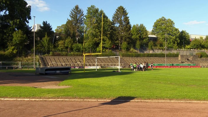 Das Solinger Stadion Jahnkampfbahn mit Blick auf das Fußballfeld und die Tribüne. Auf dem Rasen hat sich ein Team versammelt.