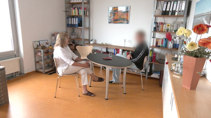 Ein unkenntlich gemachter Mann, der in seiner Kindheit Opfer sexuellen Missbrauchs wurde, sitzt gemeinsam mit seiner Anwältin an einem runden Tisch.