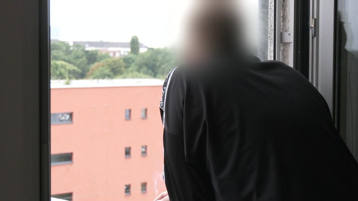 Ein junger Mann, welcher in seinem Leben Opfer sexuellen Missbrauchs wurde, schaut aus einem Fenster heraus auf weitere Gebäude. Er ist von hinten zusehen und zusätzlich unkenntlich gemacht.