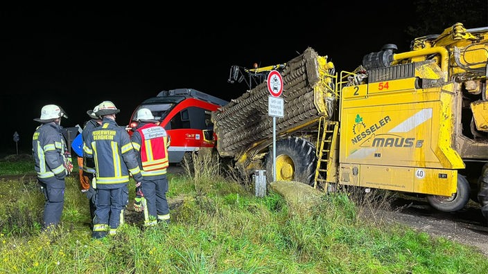 Bahn in Bergheim stößt gegen eine Erntemaschine, Feuerwehrleute stehen im Vordergrund