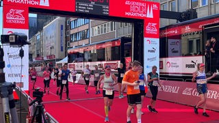 Menschen laufen über das Ziel beim Köln Marathon 2023. Sie jubeln und sind begeistert.
