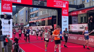 Menschen laufen über das Ziel beim Köln Marathon 2023. Sie jubeln und sind begeistert.