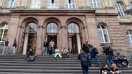 Studierende sitzen auf der Treppe am Eingang zum Hauptgebäude der RWTH Aachen.
