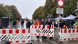 Zahlreiche Menschen sind an einer Baustelle versammelt, vor der ihnen sind Absperrungen.