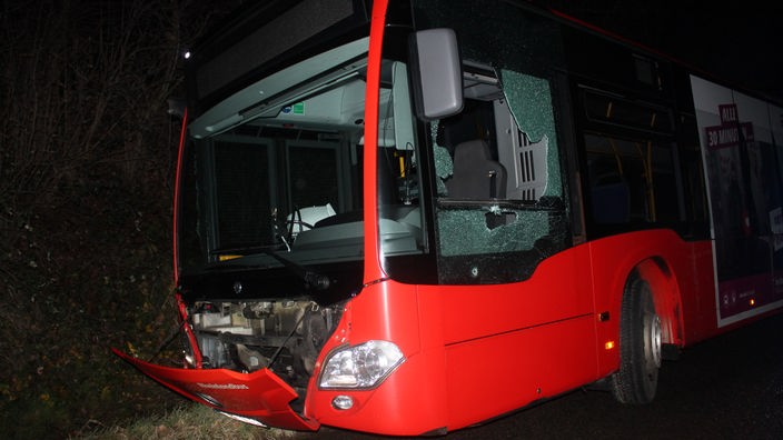 Vorderseite eines roten Linienbusses mit demolierten Glasscheiben und offener Motorklappe