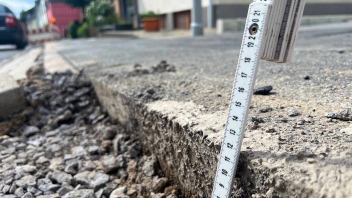 Ein Zollstock zeigt einen 12 cm tiefen Spalt im Bürgersteig