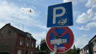 Ein Parkplatz-Straßenschild, darunter ein Halteverbotsschild, in der Luft ist im Hintergrund ein Flugzeug zu sehen