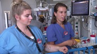 Zwei Frauen in medizinischer Arbeitskleidung, links Tabea, Kinderkrankenpflegerin und rechts Isabel, Assistenzärztin.