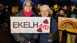 Zu sehen sind zwei Demonstrierende vor einer Menge weiterer Demonstrierender in Paderborn. Sie halten ein Plakat hoch, mit einem Slogan gegen die AfD.