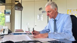Rolf Schumacher, der Bürgermeister von Alfter, sitzt am Schreibtisch und unterzeichnet ein Dokument