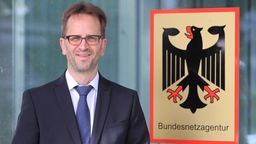 Man sieht den neuen Präsidenten Klaus Müller vor dem Emblem der Bundesnetzagentur.