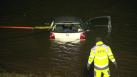 Ein Mitarbeiter des ADAC steht vor dem Auto im Wasser.