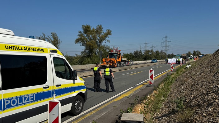 Zwei Polizisten stehen auf der Autobahn neben einem Wagen mit der Aufschrift "Unfallaufnahme"