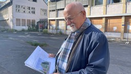 Bernhard von Grünberg hält Zettel in der Hand, auf der seine Pläne für 55 Wohnungen abgebildet sind