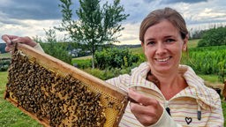 Marion Schmidt hält eine Bienenwabe in der Hand, auf der viele Bienen sitzen.