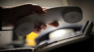 Eine Mitarbeiterin einer Telefonseelsorge greift zu einem Telefonhoere