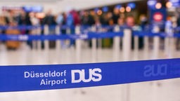 Eine Absperrung des Flughafen Düsseldorfs, mit Menschen verschwommen im Hintergrund.