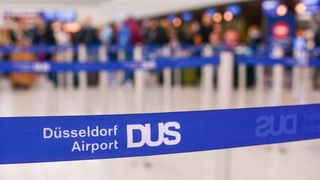 Eine Absperrung des Flughafen Düsseldorfs, mit Menschen verschwommen im Hintergrund.