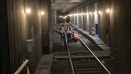 In einem beleuchteten Bahntunnel arbeiten einige Mitarbeiter der Stadtwerke an den Gleisen. Sie tragen orangefarbene Warnwesten.