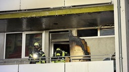 Einsatzkräfte stehen auf dem Balkon der ausgebrannten Wohnung 