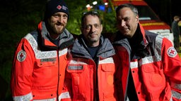Drei Männer in roten Warnjacken des Deutschen Roten Kreuz stehen in der nacht im Wald.