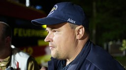 Ein Mann mt blauer Kappe ist im Profil zu sehen. Er schaut sich in der Nacht eine Einsatzstelle der Feuerwehr im Wald an.
