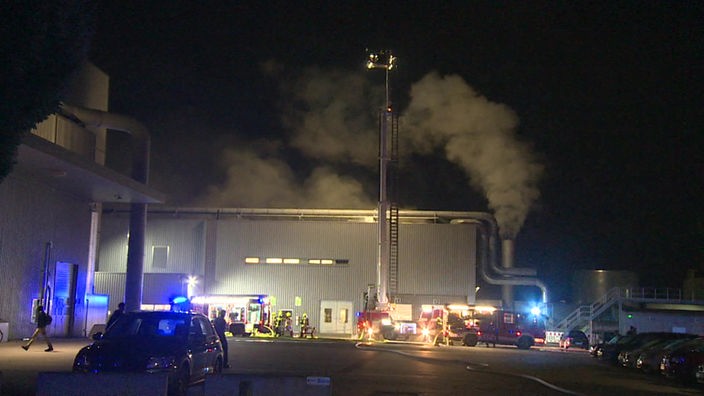 Rauch steigt aus einem Gebäude auf, davor Löschzüge der Feuerwehr.