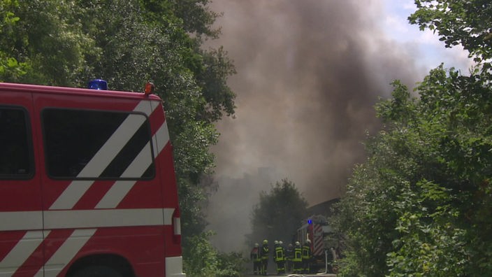 Feuerwehrleute arbeiten in dichtem Rauch vor der Lagerhalle