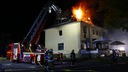 Ein Wohnhaus steht in Flammen, drum herum sind Feuerwehrmänner.