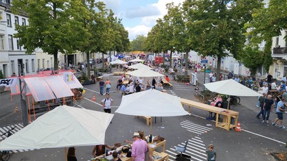 Auf einer Straße stehen und sitzen viele Menschen an Tischen und brunchen gemeinsam