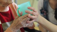  Eine Pflegekraft hilft einer alten Frau beim Trinken aus einem Becher in einem Seniorenheim.