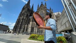 Cemal mit Instrument in der Hand, im Hintergrund der Kölner Dom
