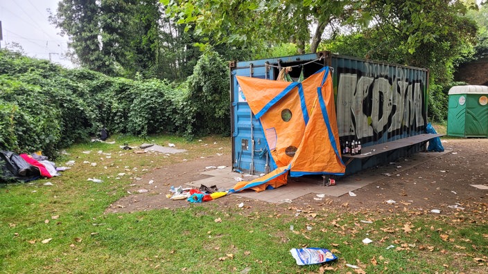 Ein alter Seecontainer mit Planen behangen, rund herum liegt jede Menge Müll auf dem Boden verteilt