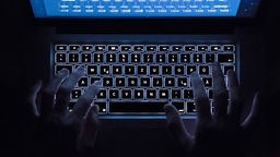 Finger Tippen auf eine beleuchtete Laptop-Tatstatur