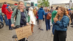 Eine junge Frau hält ein Schild mit der Aufschrift "Max, das ist veraltet wie das Fax". 