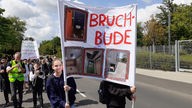 Eine Schülerin mit einem Plakat, auf dem Fotos und das Wort "Bruchbude" zu sehen ist.