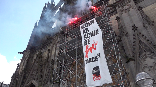 Menschen mit Transparent und bengalischem Feuer auf Baugerüst vor dem Kölner Dom 