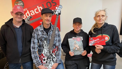 Vier Personen nebeneinander, eine mit einer Gitarre, eine mit einer Zeitung und eine mit einem roten Flyer