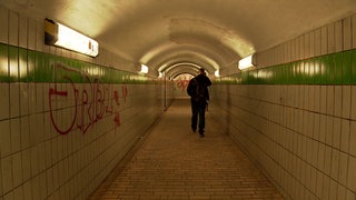 Ein Mann läuft durch einen schwach beleuchteten und verdreckten Bahnhofstunnel