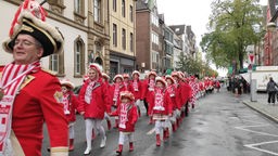 Auf dem Foto sind Menschen in roten Karnevalskostümen, die in einer Reihe eine Straße entlanggehen.