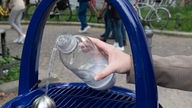 Auf dem Foto ist ein Trinkwasserspender, aus dem Wasser sprudelt. Eine Person fängt das Wasser mit einer Flasche auf.