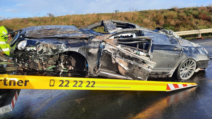 Auf dem Foto ist ein komplett deformierter Sportwagen der Marke Bentley, der gerade abgeschleppt wird.