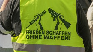 Auf dem Foto ist eine gelbe Warnweste, auf der steht "Frieden schaffen ohne Waffen"
