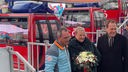 Auf dem Foto steht das Brautpaar mit einem Blumenstrauß vor den Gondeln des Riesenrads. Daneben steht Oberbürgermeister Stephan Keller.