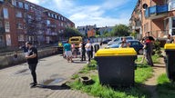 Gruppe von Erwachsenen und Kindern vor Hauseingängen, dazwischen große Müllcontainer