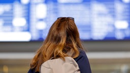 Frau steht vor Zugtafel am Kölner Hauptbahnhof